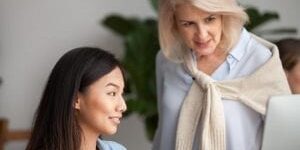 woman looking at computer screen while another woman is working at the computer